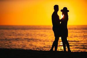 Romantic couple on the beach at colorful sunset on background photo