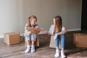 Beautiful young girls moving in new house with cardboard boxes and having fun together photo