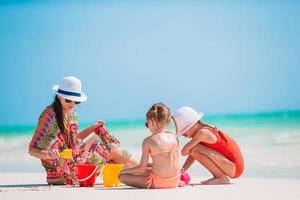 Mother and little daughters making sand castle at tropical beach photo