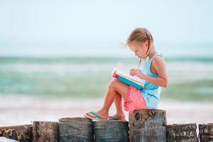 Little adorable girl reading book during tropical white beach photo