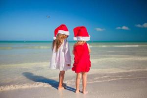 vista trasera de niñas lindas con sombreros de navidad en la playa exótica foto