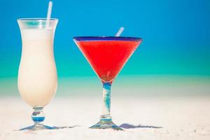 Two cocktails, pina colada and strawberry margarita on white sand beach photo