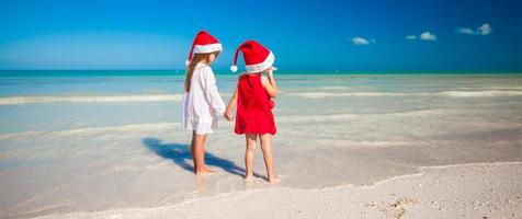 Little cute girls in Christmas hats on the exotic beach photo