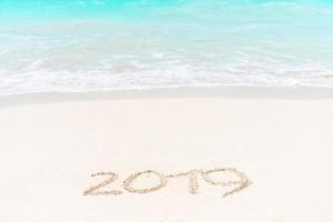 2019 handwritten on sandy beach with soft ocean wave on background photo