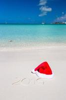 2016 escrito en la playa tropical de arena blanca con sombrero de Navidad foto