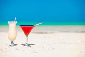 Two cocktails, pina colada and strawberry margarita on white sand beach photo