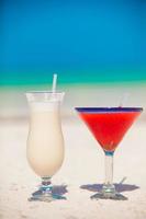 Two cocktails, pina colada and strawberry margarita on white sand beach photo