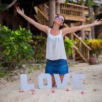 Young girl sitting on sand with the word Love and spread her arms photo