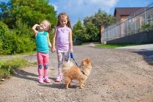 Two Little girls walking with small dog on a leash outdoor photo