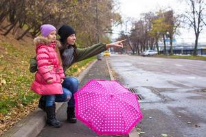 Little girl and her mother walking with umbrella on a rainy day photo