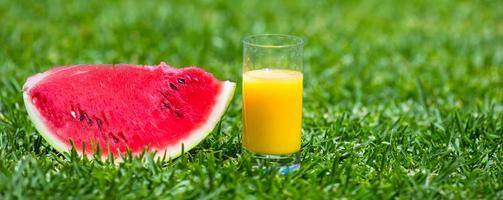 verano y tema fresco sandía rebanada madura roja y vaso de jugo de naranja sobre hierba verde foto