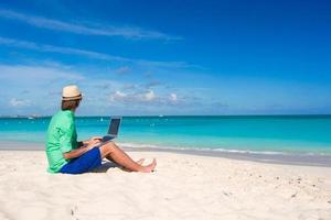 Young man working on laptop at tropical beach photo