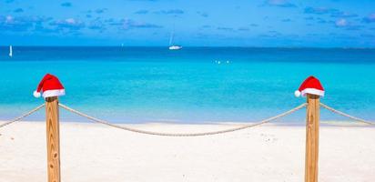 primer plano dos sombreros de santa en la valla en la playa blanca tropical foto