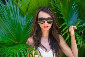 Portrait of young beautiful woman against green palm trees photo