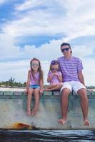 familia de tres en un muelle de madera disfrutando de la vista al mar foto