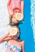 Little girls covering eyes with lemon halves near eyes on background swimming pool photo