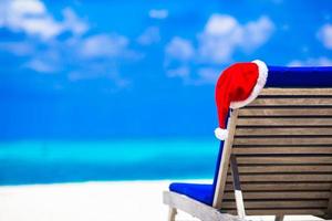 Sun chair lounge with red Santa Hat on tropical white beach and turquoise water photo