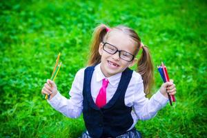 Portrait of adorable little school girl in glasses with pencils outdoor photo