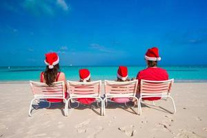 Happy family of four on beach in red Santa hats photo
