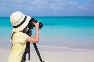 Little girl with camera on a tripod at white sandy beach photo