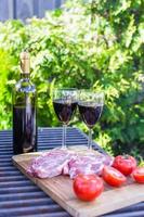 Bottle of red wine, steak and tomatoes on barbecue outdoors photo