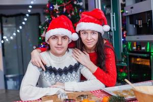 Portrait of young happy couple baking Christmas cakes at home in Santa hat photo