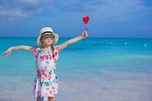 Little girl with red heart in hands on a tropical beach photo