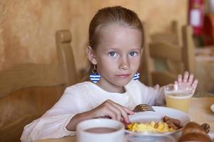 Adorable little girl having breakfast at indoor cafe photo