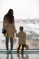 Mother and little daughter looking out the window at airport terminal photo