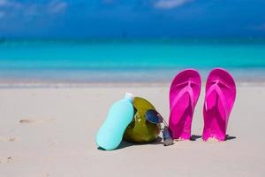 Flip flops, coconut and suncream on white sand photo