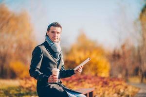 Young man drinking coffee with phone in autumn park outdoors photo