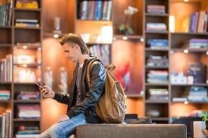 Young positive man picking new book on shelves in bookstore photo