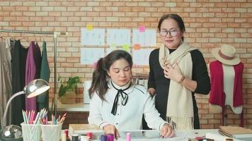 equipo de moda, diseñadora asiática y asistente adolescente en el estudio, brazos cruzados y sonrisa, feliz trabajando con hilos coloridos y costura para el diseño de vestidos, boutique profesional sastre pyme emprendedora. video