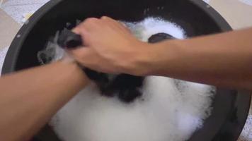 bijgesneden handen van persoon sjerpen wasserij in een emmer. het wassen kleren door hand- met wasmiddel. man's hand- in een eerste persoon visie het wassen een vuil overhemd in een plastic bassin. video