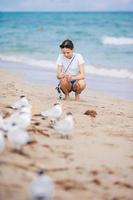 niña adolescente feliz jugando con pájaros de gaviota, corriendo y divirtiéndose en la playa en un caluroso día de verano. florida vacaciones de verano vacaciones foto