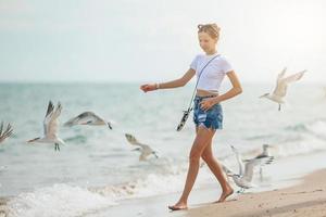 niña adolescente feliz jugando con aves gaviotas, corriendo y divirtiéndose en la playa en un caluroso día de verano. florida vacaciones de verano vacaciones foto