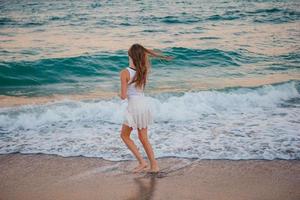 Adorable girl have fun on the beach is shallow water at sunset photo