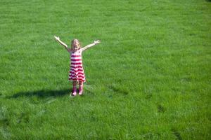 Beautiful little girl spread her arms standing on the lawn photo