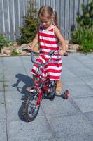 niña linda monta una bicicleta en el vestido en el patio foto