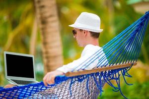 Young man with laptop at hammock on tropical vacation photo