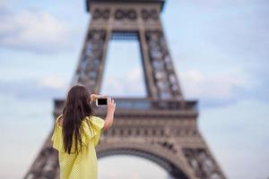 Young woman making photo by phone background Eiffel Tower in Paris