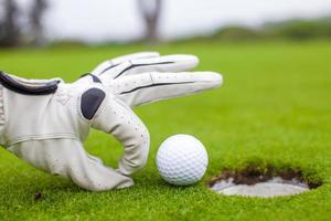 primer plano de la mano de un hombre poniendo una pelota de golf en el hoyo en curso foto