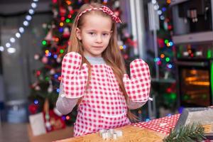 Adorable little girl in wore mittens baking Christmas gingerbread cookies photo