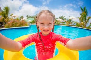 Little girl making selfie at inflatable rubber ring in swimming pool photo