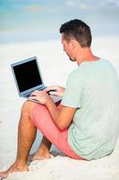 Young man with tablet computer during tropical beach vacation photo