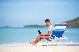 Young man with tablet computer during tropical beach vacation photo