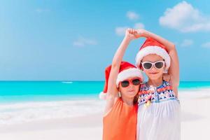 Little adorable girls in Santa hats during beach Christmas vacation having fun together photo