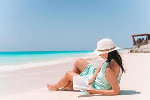 mujer joven leyendo un libro en el chaise-lounge en la playa foto