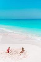 Adorable little kids play with sand on the white beach photo