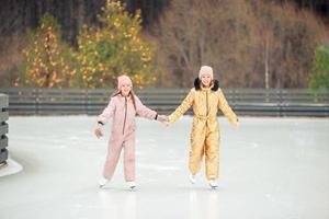 chicas adorables patinando en la pista de hielo al aire libre en el día de nieve de invierno foto